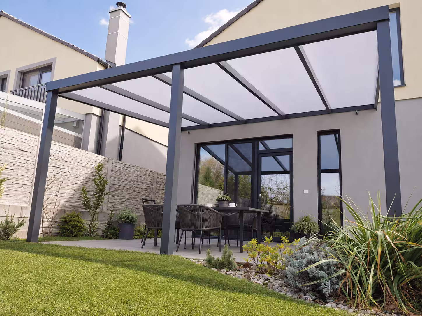 Antracitová hliníková pergola Basic Class s mliečnou strechou pri dome s komínom