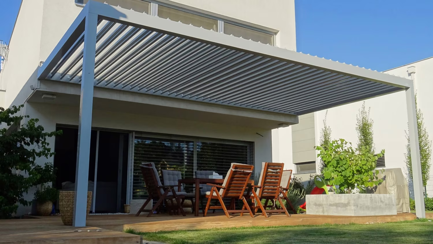 Bioklimatická hliníková pergola s natáčacími lamelami nad terasou s jedálenským sedením pri modernom dome