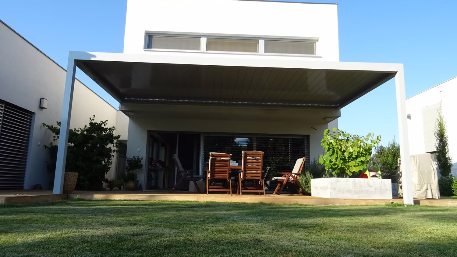 Bioklimatická hliníková pergola nad terasou so sedením pri modernom bielom dome