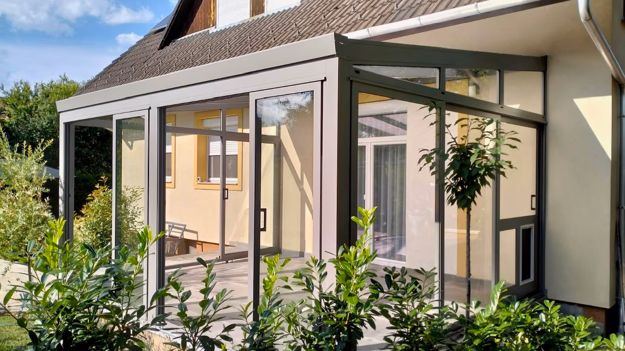 Zimná záhrada Economic Garden s posuvnými presklenými dverami pri žltom rodinnom dome