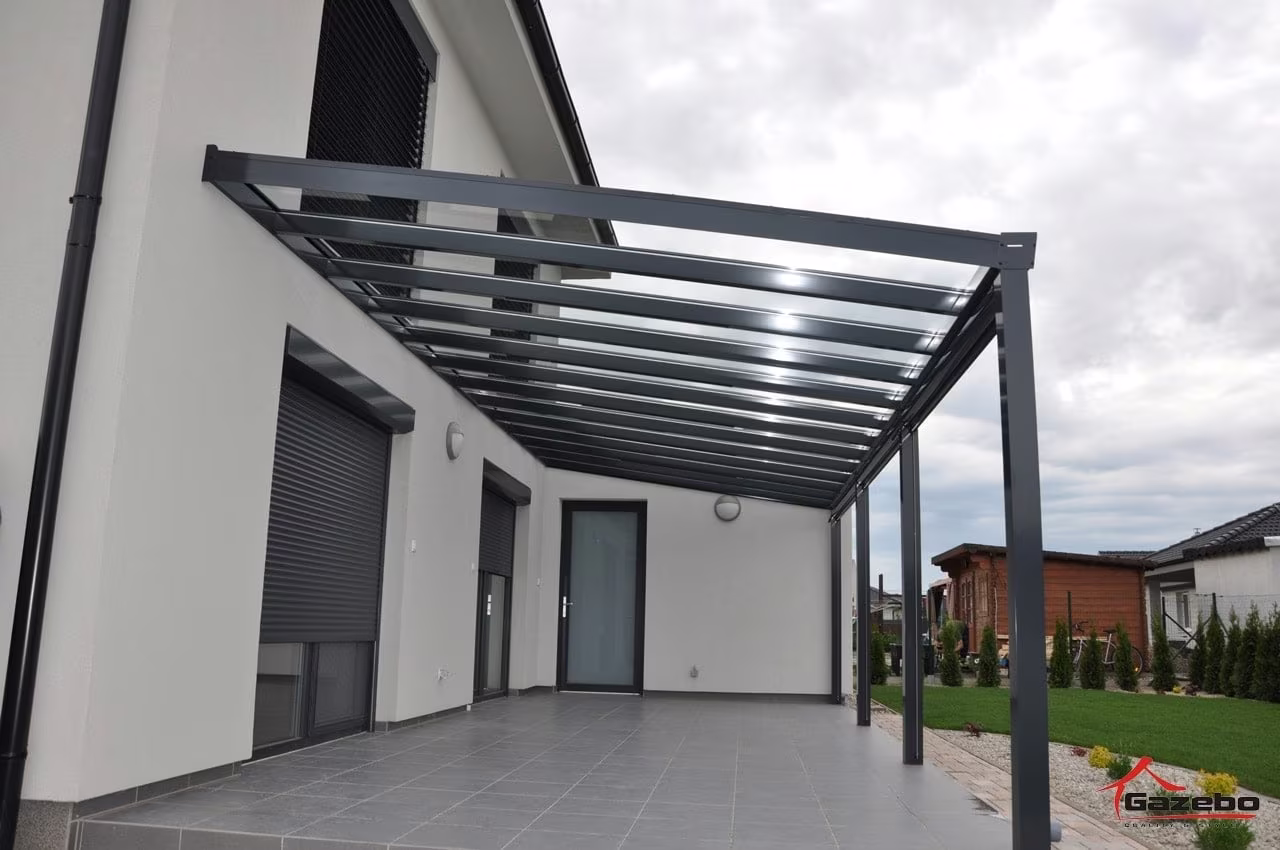 Antracitová hliníková pergola Top Class nad dláždenou terasou pozdĺž domu s roletami