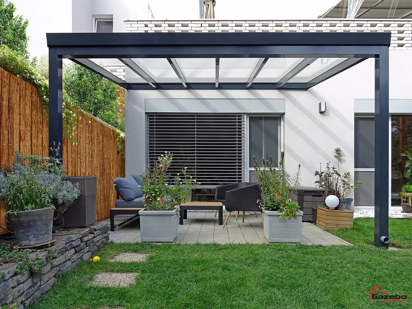 Antracitová hliníková pergola Top Class nad terasou so sedením pri dome s dreveným plotom