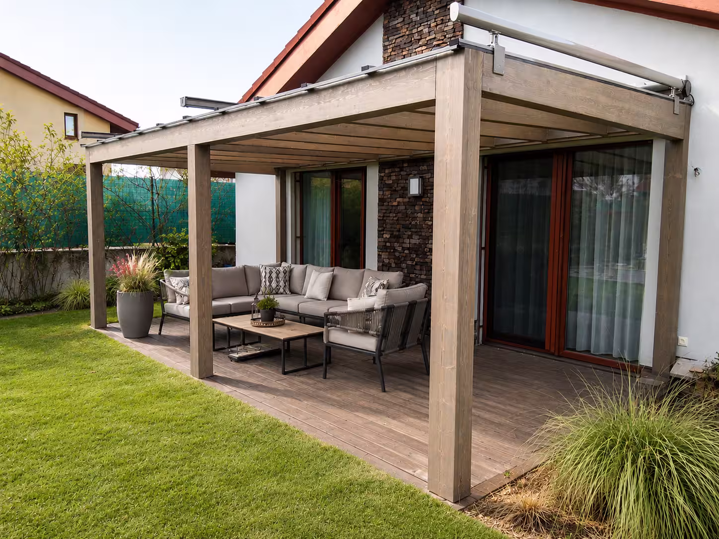 Drevená pergola Milano pri kamennej fasáde so sivým záhradným posedením
