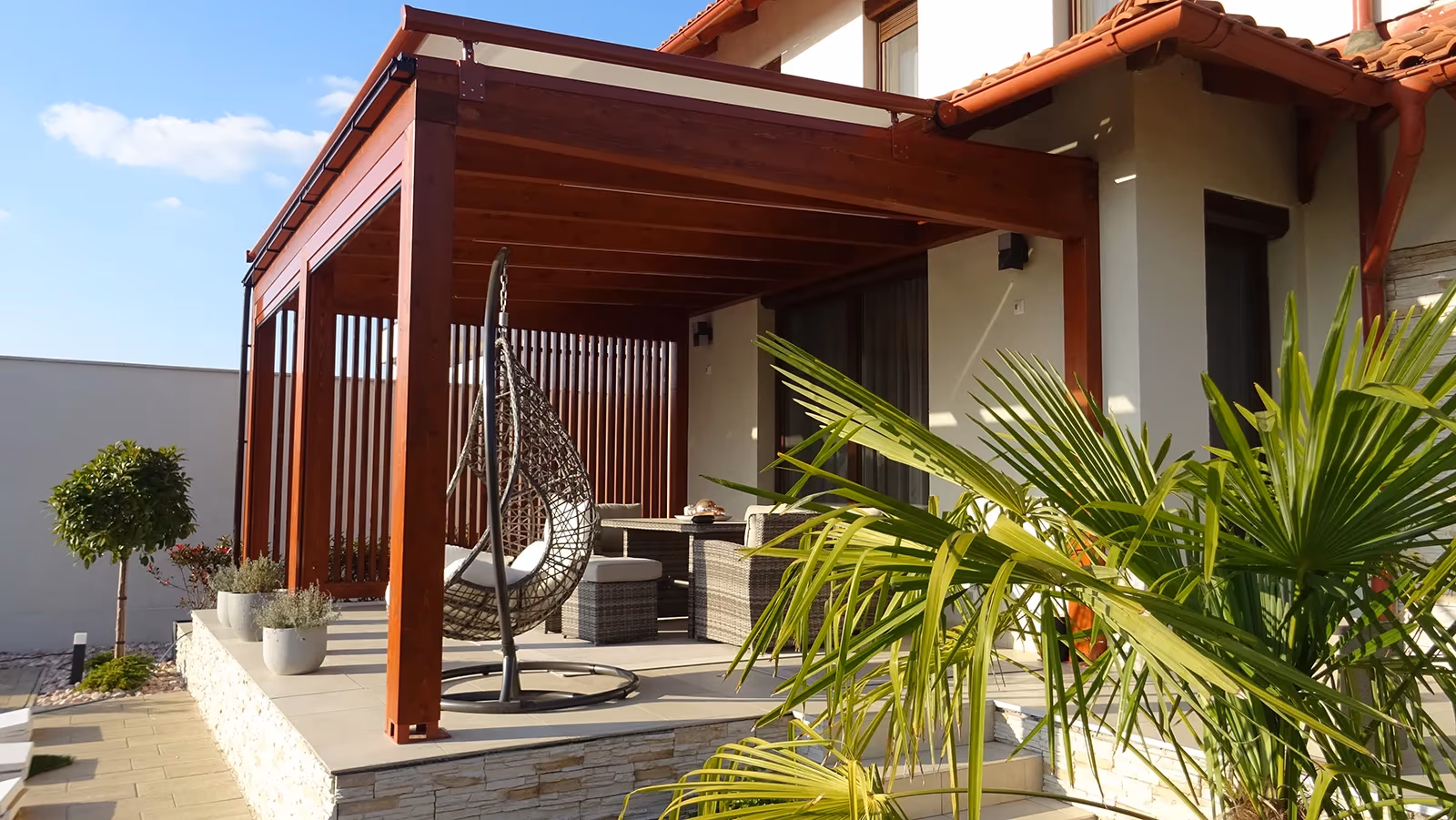 Drevená pergola Milano so zaveseným kreslom a palmou