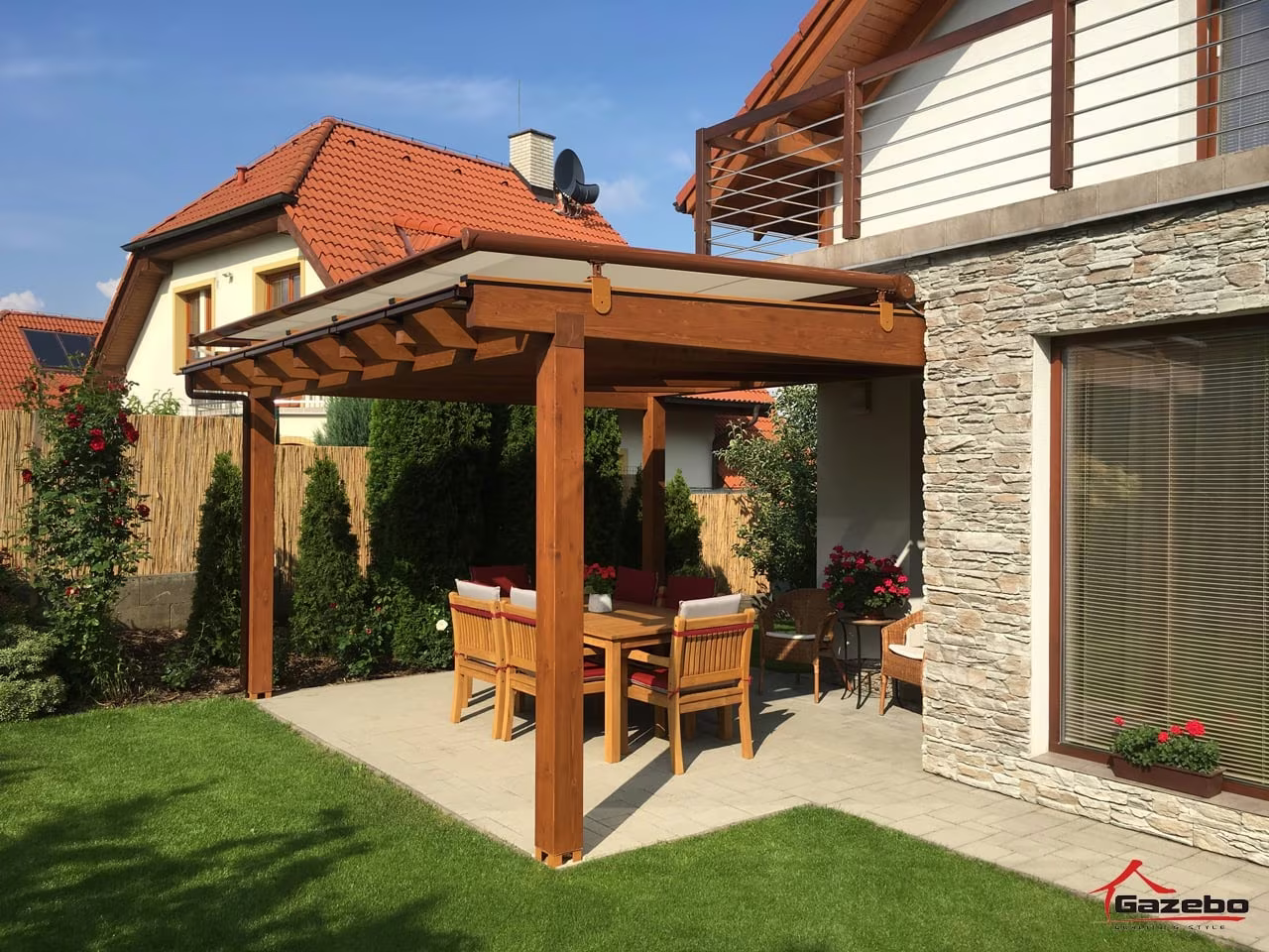 Drevená pergola Fénix nad dláždenou terasou s jedálenským sedením pri dome s kamenným obkladom